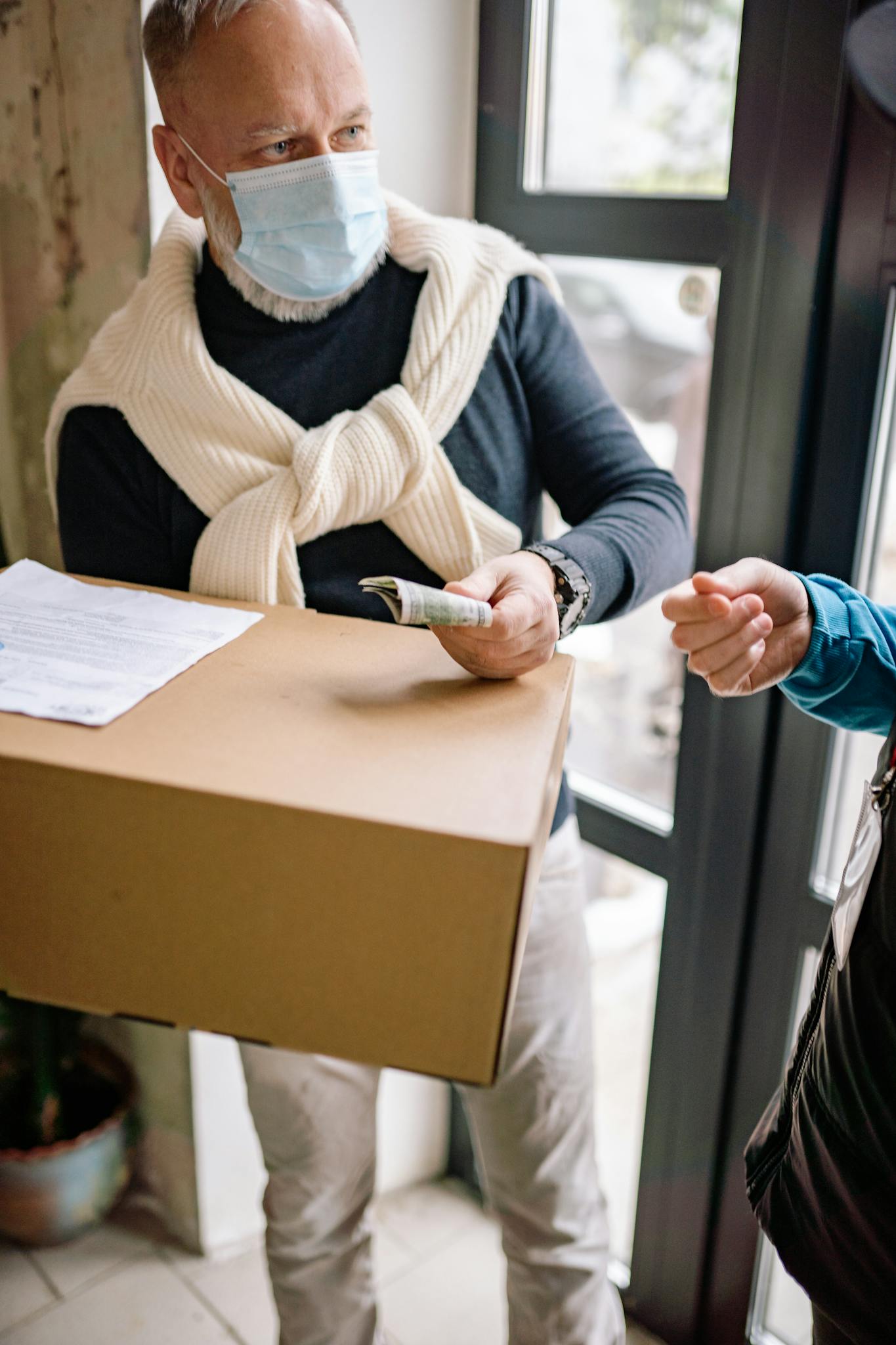 Senior man with facemask receiving a package and making payment indoors.
